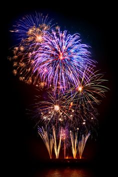 fireworks are lit up in the night sky over water with reflections on the water surface