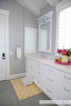 a bathroom with gray walls and yellow rugs on the floor next to white cabinets