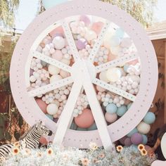 a pink ferris wheel surrounded by balloons and other decorations in front of a house with a zebra standing next to it