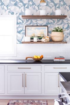 a kitchen with white cabinets and blue wallpaper on the walls, along with a bowl of fruit