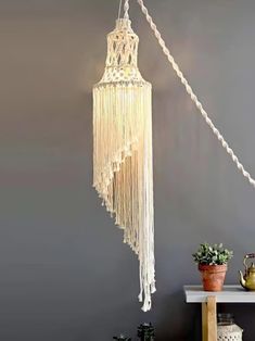 a white lamp hanging from the side of a wall next to a potted plant