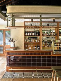 a bar with lots of bottles and glasses on the shelves above it, along with two stools