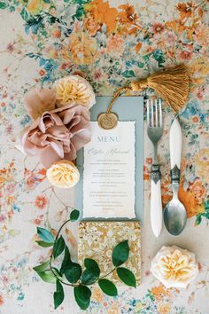 a table setting with flowers, silverware and menu cards on it's side