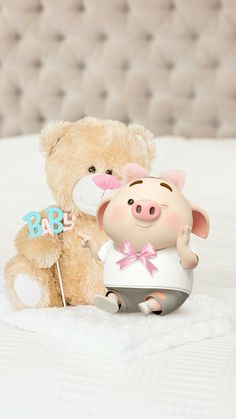 a teddy bear sitting next to a stuffed pig holding a baby cake topper on a bed