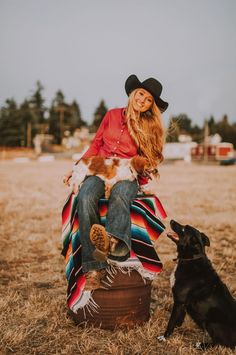 a woman in a cowboy hat sitting on top of a suitcase next to a dog