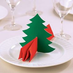 a paper christmas tree sitting on top of a white plate next to empty wine glasses