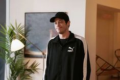 a man in a black jacket and hat standing next to a potted plant