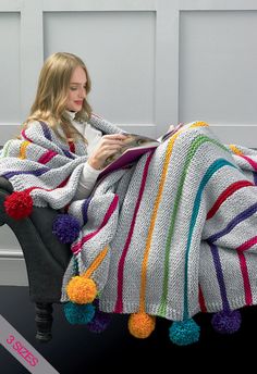 a woman sitting in a chair under a blanket with pom poms on it