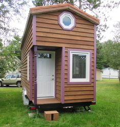 a tiny house on wheels in the middle of a grassy area with a door and window