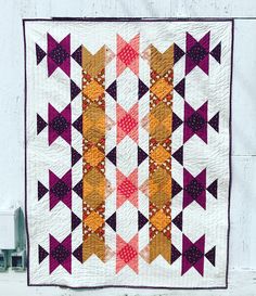 a quilted wall hanging on the side of a white building with an orange and purple design