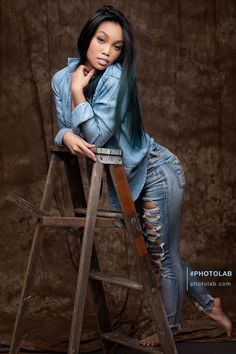 a woman sitting on top of a wooden ladder posing for a photo with her hand on her chin