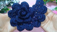 a crocheted blue flower is being held in someone's hand with christmas decorations behind it