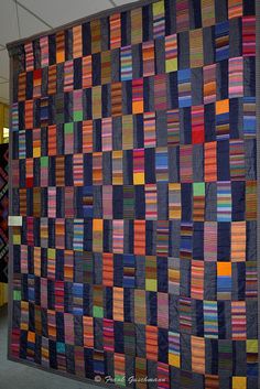 a large quilt hanging on the wall in an office building, with multiple rows of different colors