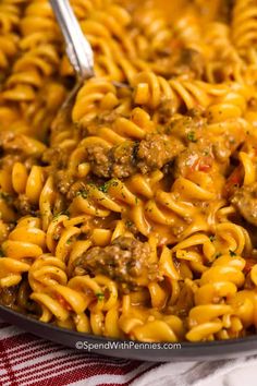 a skillet full of pasta with meat and gravy in it on a red and white checkered table cloth