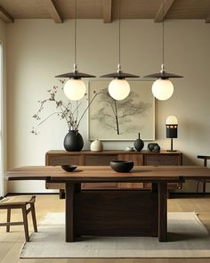 a dining room table with four lights hanging from it's ceiling and two vases on the table