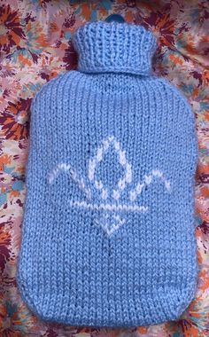 a blue knitted hot water bottle cover on a floral background with the word'love'written in white