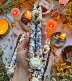 a person holding an item in their hand with candles and flowers on the table behind it