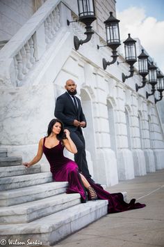 a man and woman in formal wear sitting on the steps of a building with their arms around each other