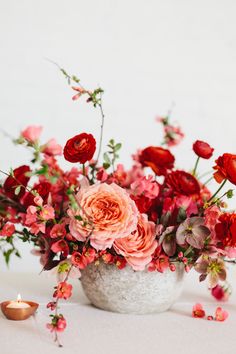 a vase filled with pink and red flowers on top of a white table next to a candle