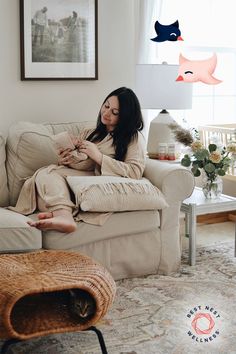 a woman sitting on top of a couch in a living room next to a cat