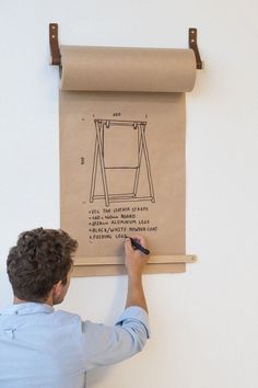 a man is drawing on a piece of paper with a roller attached to the wall