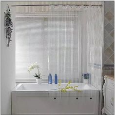 a white bath tub sitting under a window next to a sink with flowers in it