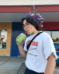 a young man is drinking from a green cup while standing on a bench in front of a store