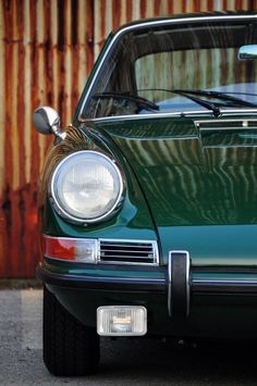 an old green car parked in front of a rusted metal wall with the door open