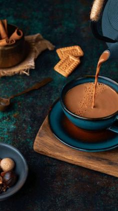 a cup of hot chocolate being poured into a mug with nuts and cinnamons on the side