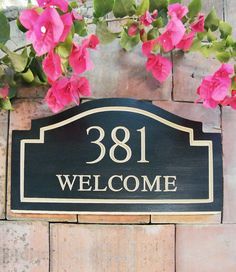 a black and white welcome sign with pink flowers in front of it on a brick wall