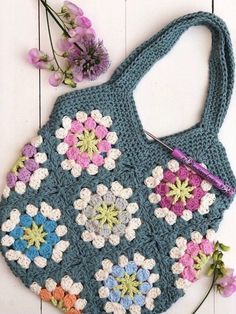 a crocheted bag sitting on top of a white table next to purple flowers