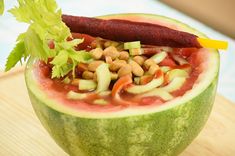 a watermelon filled with food and garnish on top of a wooden table