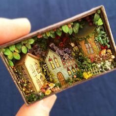 someone holding up a miniature house made out of paper and wood with flowers on it