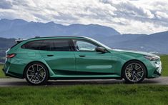 a green car parked on the side of a road in front of some grass and mountains