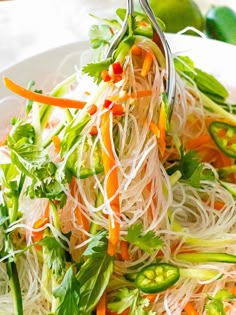 a white plate topped with veggies and noodles next to limes on a table