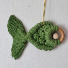 a green crocheted fish ornament hanging from a gold chain on a white wall