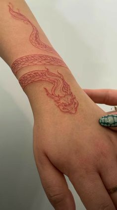 a woman's hand with a dragon tattoo on her left wrist and a snake ring