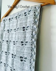 a crocheted blanket hanging on a wooden hanger next to a white wall