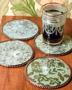 four glass coasters sitting on top of a wooden table next to a cup filled with liquid