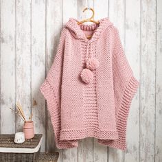 a pink knitted sweater hanging on a wooden wall next to a basket and potted plant