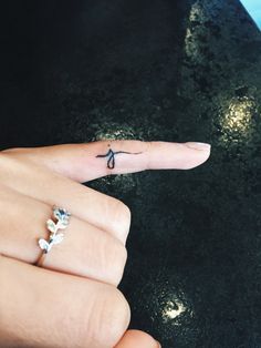 a person's left hand with a tiny cross tattoo on the thumb and finger