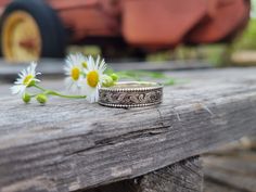 two wedding rings sitting on top of a wooden table with daisies in the foreground