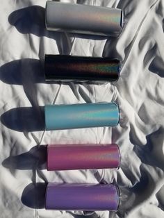 four different colors of lipstick sitting on top of a white sheeted bed next to each other