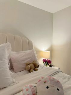 a teddy bear sitting on top of a white bed next to pillows and a lamp