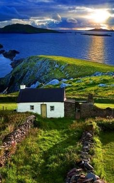 a small white house sitting on top of a lush green hillside next to the ocean