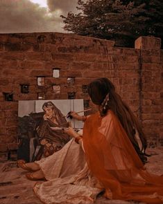 a woman sitting on the ground next to a brick wall with an easel in front of her