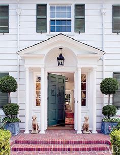 two dogs are sitting on the steps in front of a white house with green shutters