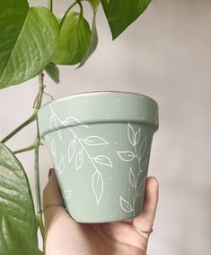 a hand holding a potted plant with leaves painted on it