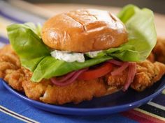 a chicken sandwich with lettuce and tomatoes on a blue plate