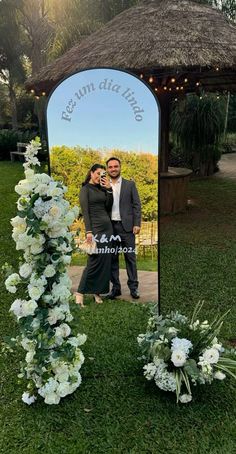 a man and woman standing in front of a mirror with flowers on the ground next to it